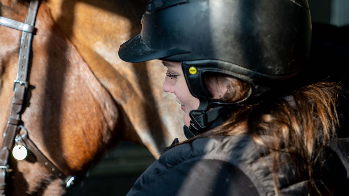 Närbild på elev med ridhjälm som står vid sidan av en häst