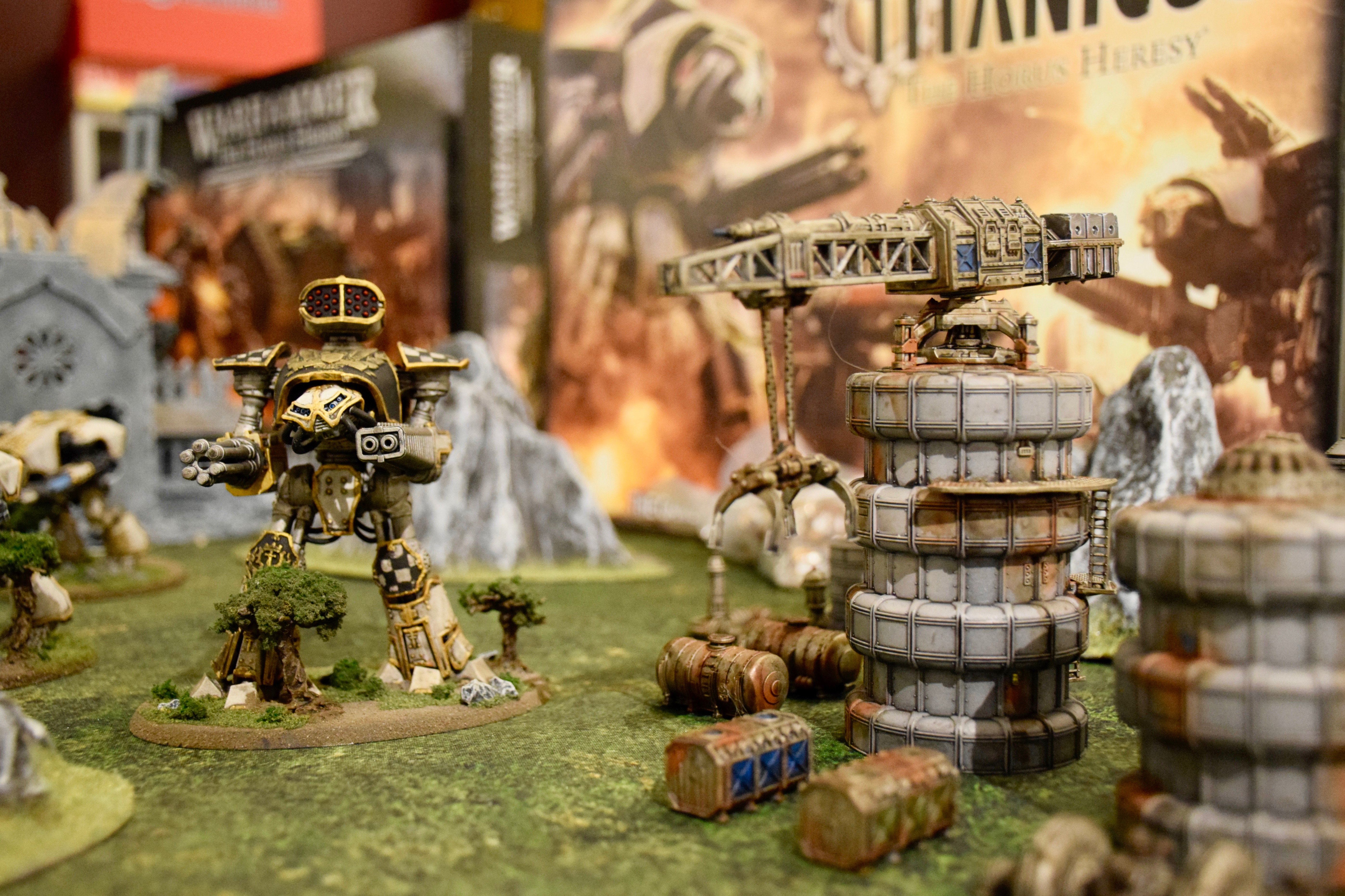 En spelfigur poserar bredvid en liten lyftkran. I bakgrunden skymtar klippformationer och framsidan av lådor som innehåller spel. 