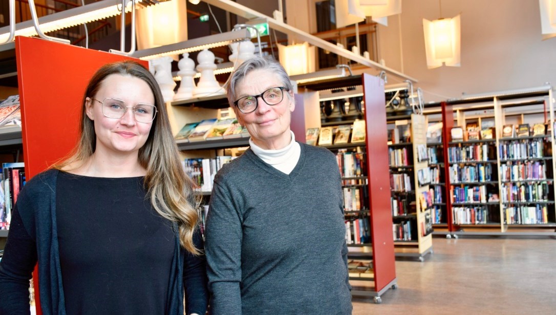 Linnéa Blomqvist har långt ljusbrunt hår och glasögon. Ann-Britt Dahl har kortklippt grått hår och glasögon. Båda bär tröjor i mörka färger, i bakgrunden syns bibliotekshyllor med böcker. 