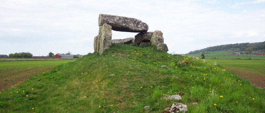 Gånggrift i Luttra, Falköpings kommun. Ett stenmonument på grön kulle i odlingslandskap.