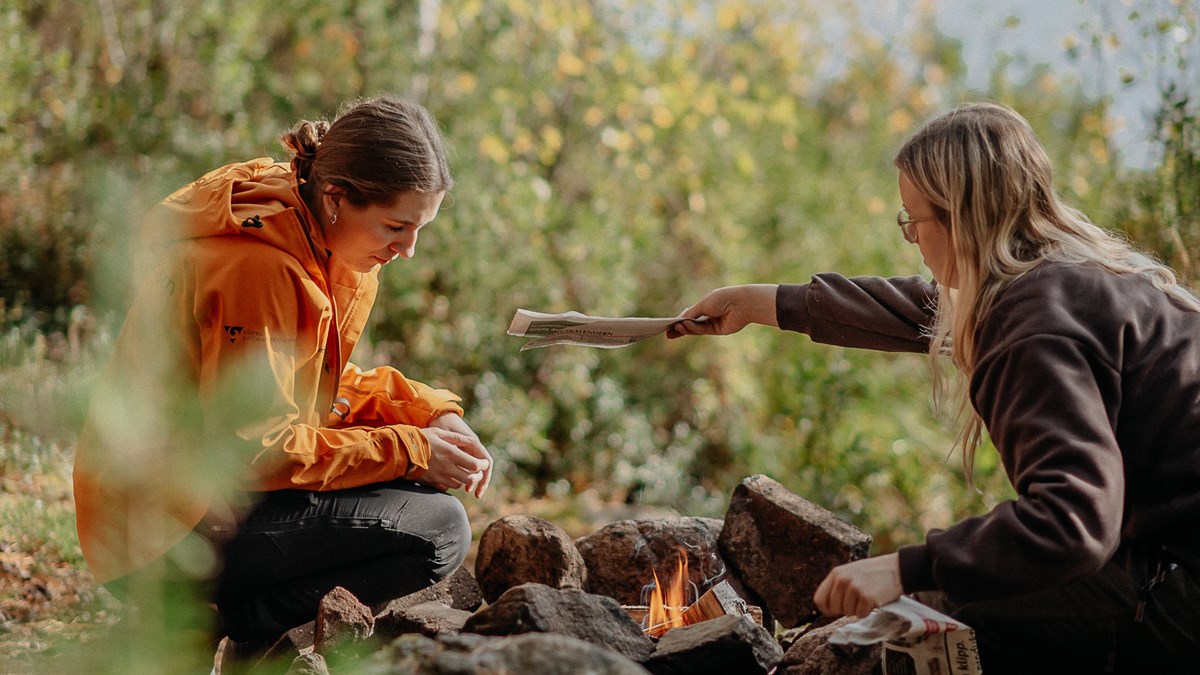 Två elever sitter framför en öppen eld i skogen
